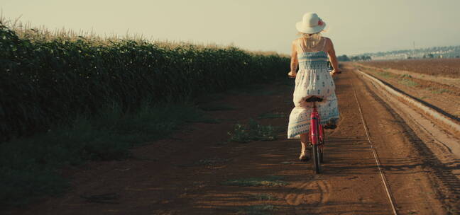 在农田土路上骑自行车的女孩