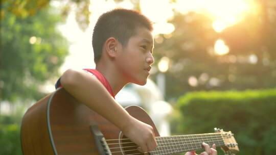 傍晚夕阳下坐在小区草地上弹吉他的小男孩