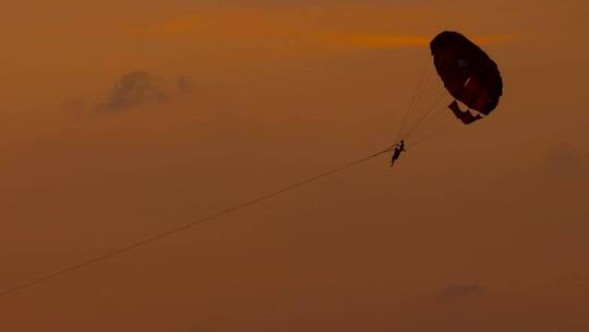 一对情侣在夕阳的风中享受滑翔伞运动_