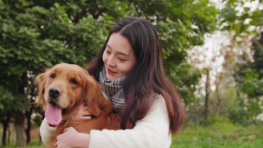 长发女青年抱着金毛犬狗狗在公园里玩耍