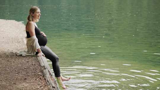 孕妇坐在湖边木板的边缘，脚在水中摆动