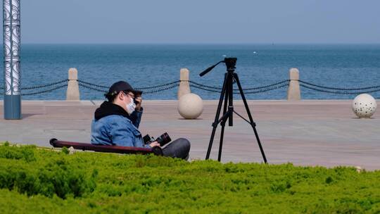 海边景区广场长椅上休息的摄影师摄像师