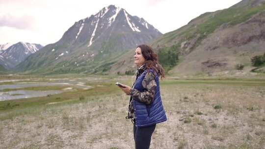 戴耳机的女游客在山脉和风景的背景下跳舞。