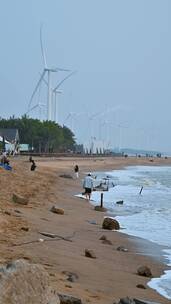 东方市鱼鳞洲沙滩上的游客与风力发电机。