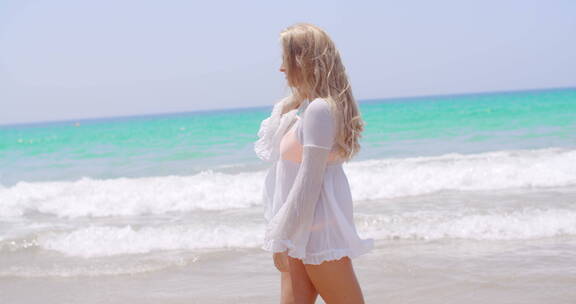 金发女孩穿着白色束腰外衣在海滩上散步
