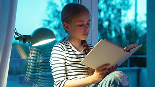女孩开着台灯坐在窗台上看书