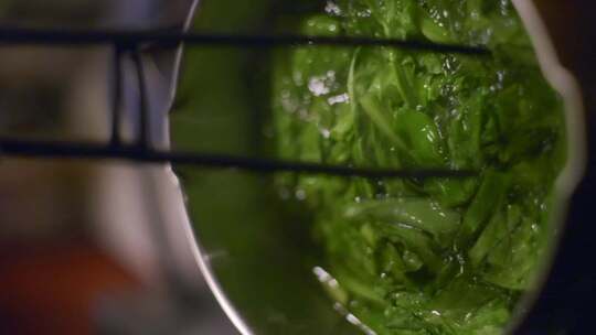 绿色蔬菜在沸水中用钳子搅拌，拍摄为垂直特