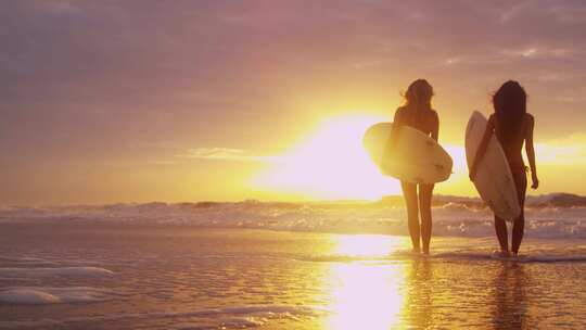 日落时分，两名名女子在沙滩上拿着冲浪板