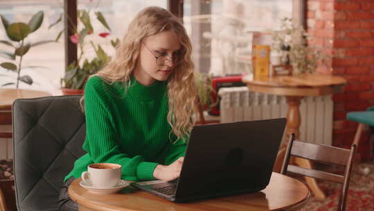 美丽的年轻女子学生在咖啡馆远程工作或学习在笔记本电脑上输入信息