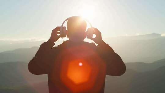 男人面向群山拿起耳机戴在头上听音乐