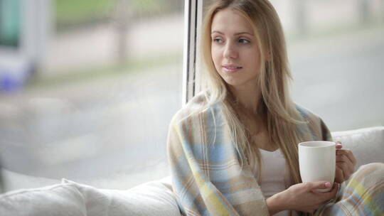 女人坐在窗边沙发上端着一杯咖啡