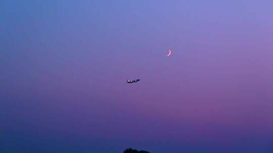 飞机飞过傍晚的月空一轮弯月