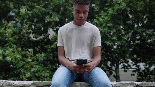 年轻的非裔美国少年男孩坐在户外使用手机视频素材模板下载