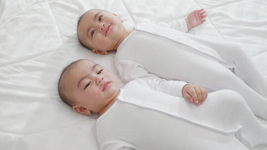 双胞胎宝宝靠在床上玩耍