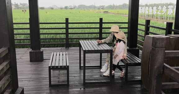妈妈与女儿在稻田木亭中休息看手机
