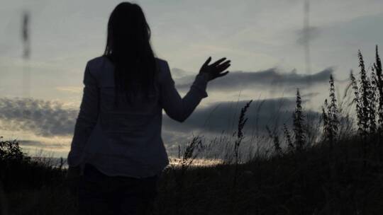 女人在夕阳下挥手告别剪影