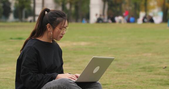 女大学生在大学校园里草地上用电脑学习