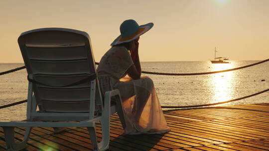 女人坐在海边的日光浴床上看海上日落