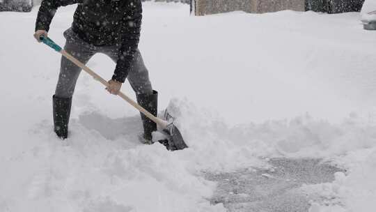 暴风雪后在车道上铲雪的人努力工作靴子清除