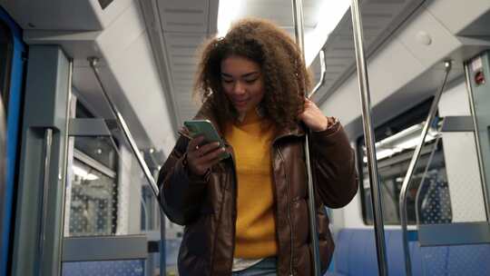 肖像开朗的非洲女性乘坐地铁并使用智能手机上网和