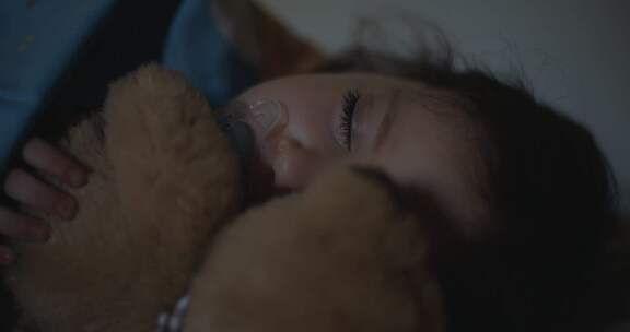 小女孩晚上躺在床上抱着她的泰迪熊睡觉