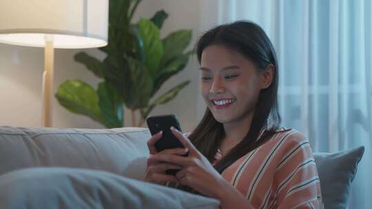 亚洲美女晚上坐在沙发上用手机聊天视频素材模板下载