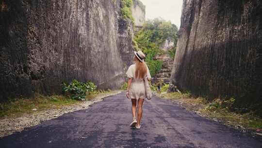 戴草帽的旅游金发女子在岩石悬崖之间的沥青