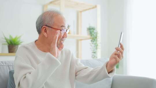 亚洲老年人在客厅使用手机进行视频通话。视频素材模板下载