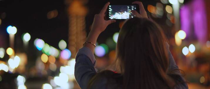 女人用手机拍摄城市夜晚美景