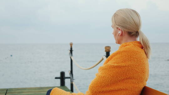 裹着毛巾的女人坐在海边用耳机听音乐