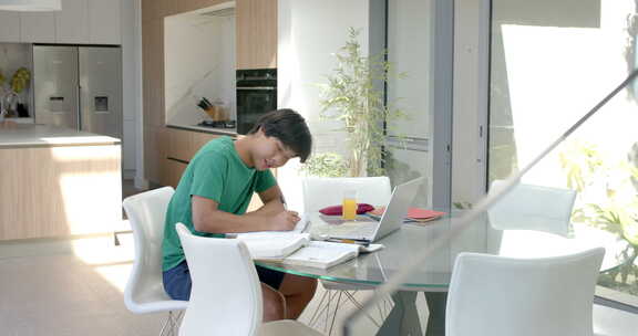 十几岁的亚洲男孩在现代家庭餐桌上用笔记本