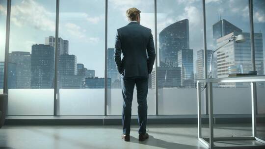 商人成功人士走向办公室窗户前俯瞰城市