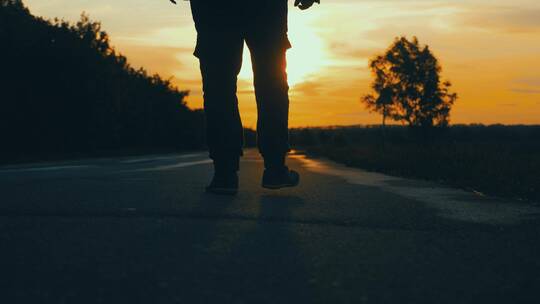 年轻人迎着夕阳走在乡间小路上的剪影