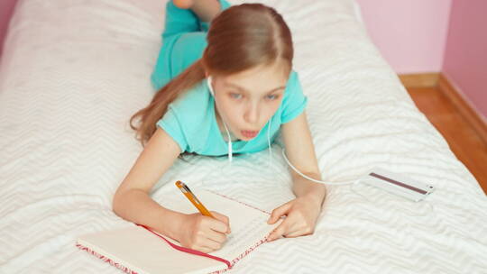 戴耳机躺在床上写字的女孩视频素材模板下载