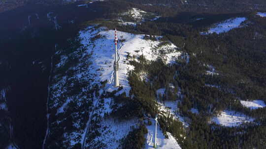 白雪覆盖的高原上风力涡轮机和广播塔的空中跟踪照片。黄金时刻