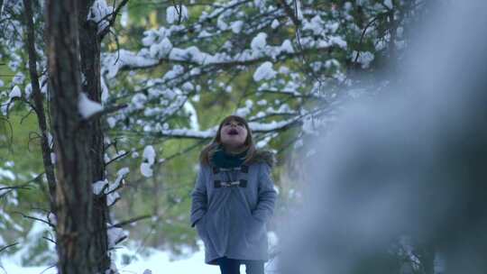 一个小女孩站在树林里，张着嘴接住飘落的雪