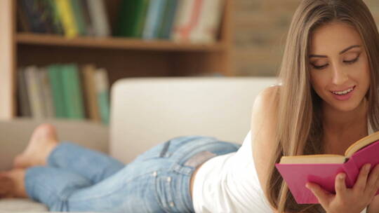迷人的年轻女子躺在沙发上看书视频素材模板下载