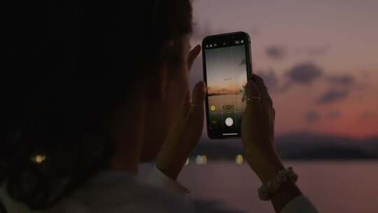 女孩拿起手机拍摄夕阳