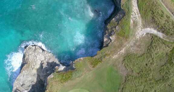 岩石海岸线的自上而下视图，绿松石清澈的海水和带沙子的绿色高尔夫球场果岭