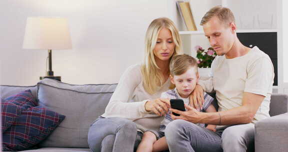 微笑的年轻美国家庭和小孩子坐在沙发上看平板电脑上的卡通快乐高加索人