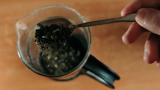 顶部视图：勺子在玻璃茶壶中加入天然草药茶