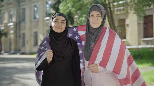 两名裹着美国国旗的穆斯林妇女看着镜头微笑。自信的肖像