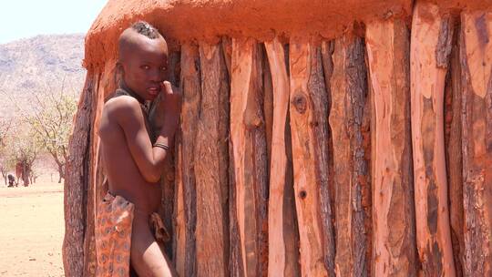 一个非洲辛巴部落男孩靠在他小屋上