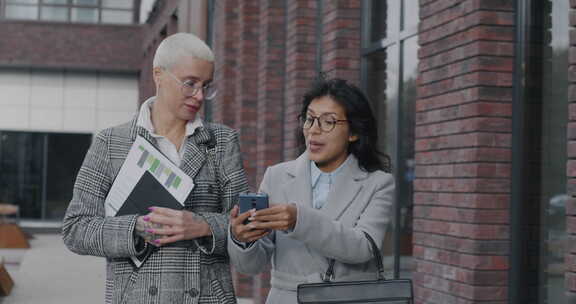 年轻女商人在城市街道上聊天和看着智能手机