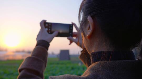 女性在夕阳下用手机拍摄照片