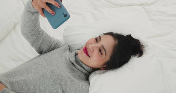 年轻女人躺在床上刷手机视频聊天