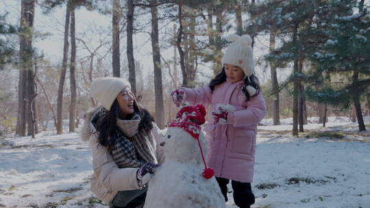 年轻妈妈和女儿在雪地里堆雪人