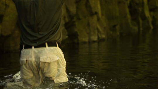 一个男人举着包裹慢慢走进河水深处