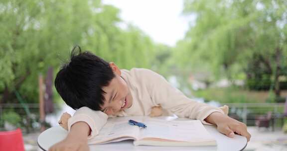 小孩在户外学习写作业累了趴在桌子上