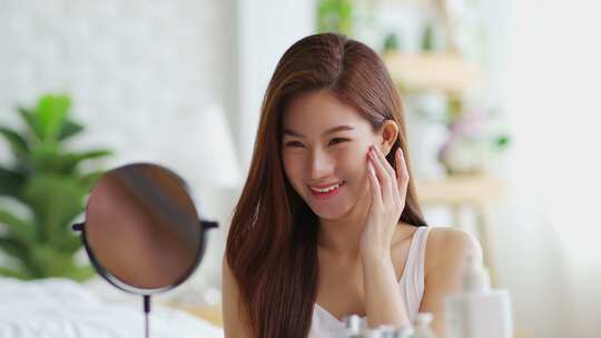 快乐的亚洲年轻女子微笑着照镜子做皮肤护理触摸脸颊和美容护理视频素材模板下载